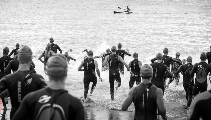 Participantes do Triatlon Paranaense saltam na água para iniciar a etapa de natação. O início de uma emocionante competição onde os nadadores se preparam para desafiar as águas e atingir os seus objetivos. Uma imagem cheia de expectativa e determinação no início do triathlon paranaense.